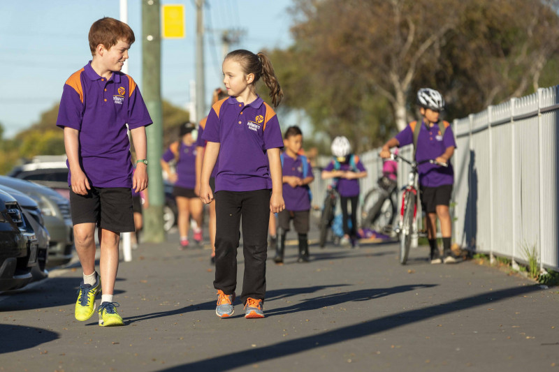 Primary school children walking to school next to a row of parked cars